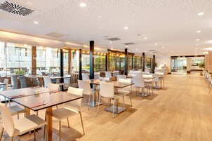 Un restaurante moderno con varias mesas y sillas, ventanas amplias y un suelo de madera pulida.