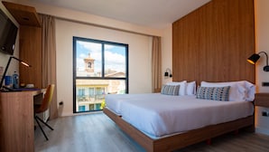 A modern hotel room with a large bed, a desk, and a view of buildings through a large window. - Hotel Isla Mallorca & Spa (Palma de Mallorca)