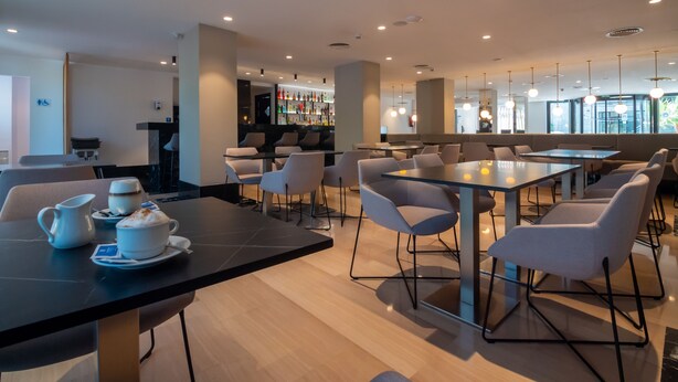 Una cafetería moderna con mesas, sillas y una barra, y vistas al exterior.