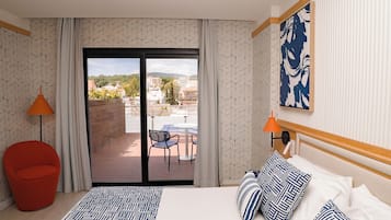 Habitación de hotel con cama, una silla roja, un balcón con mesa y sillas, y vistas a la ciudad.