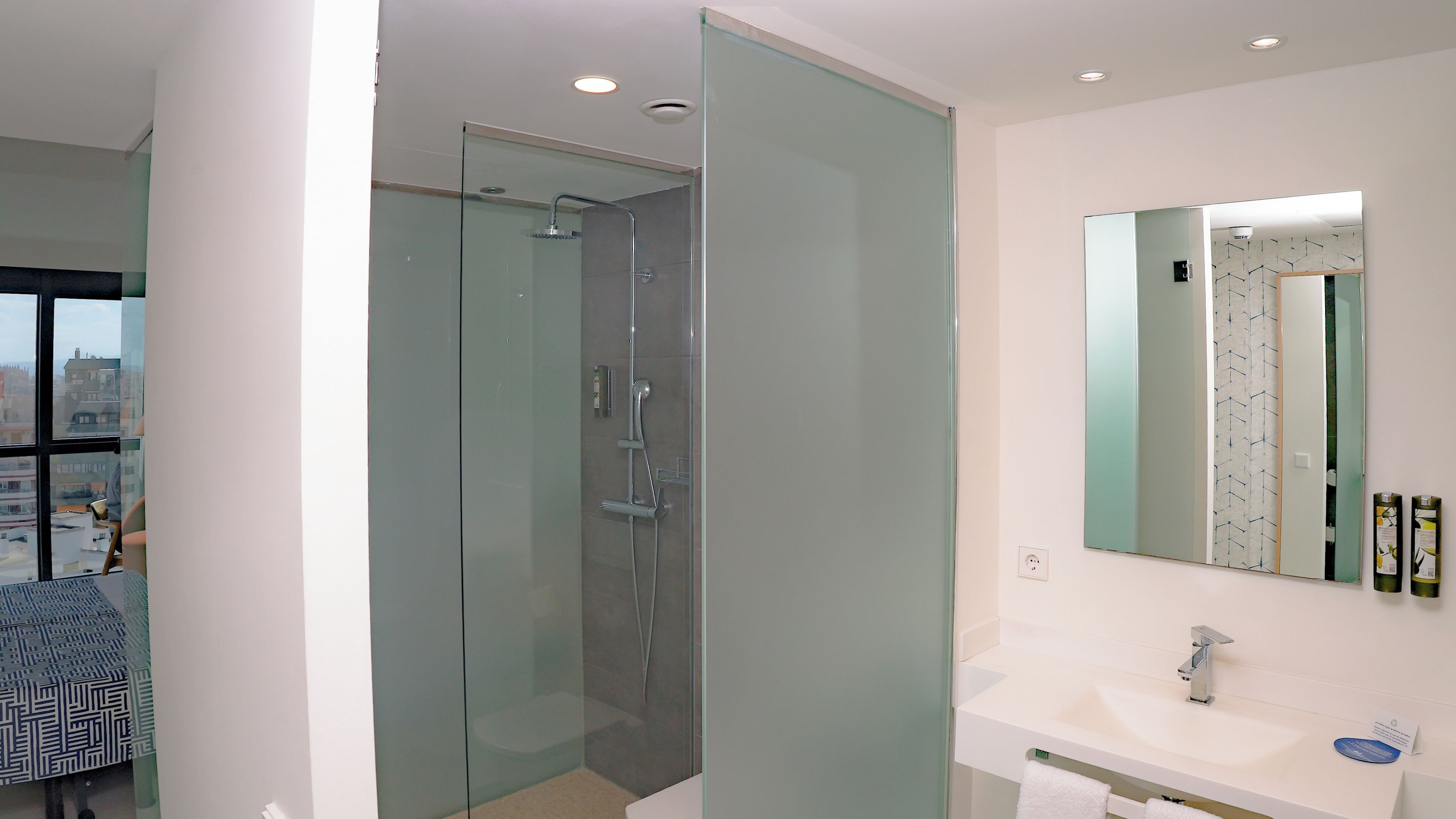 Un baño moderno con ducha envuelta en vidrio, lavamanos blanco y un espejo grande.