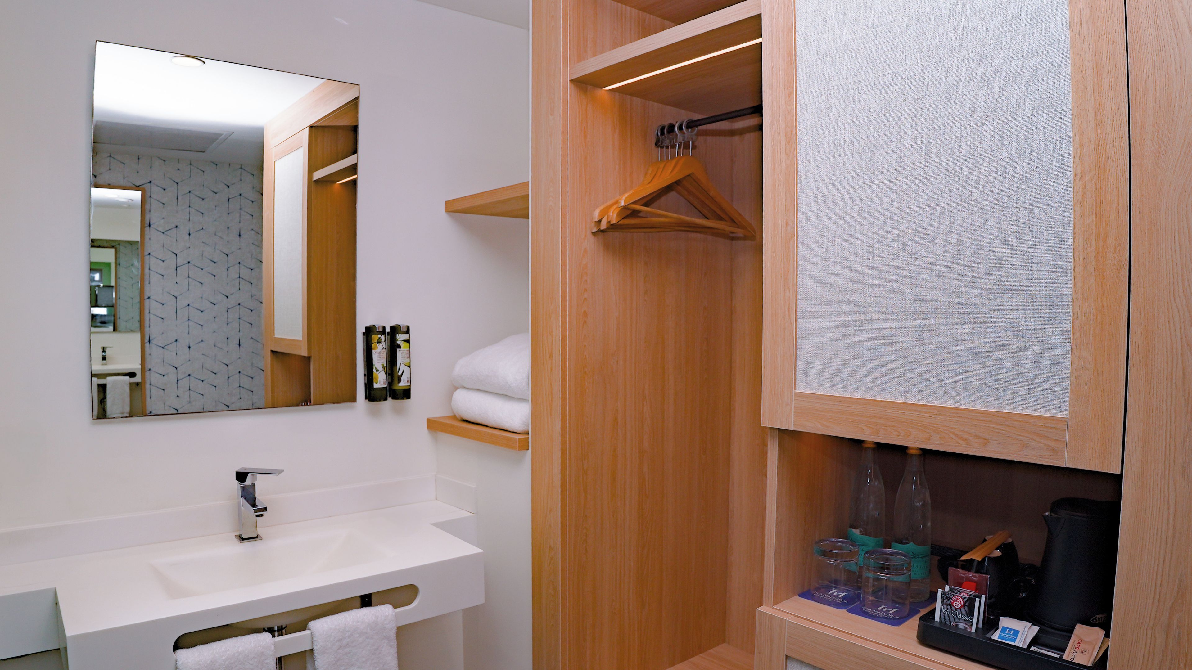 Un baño moderno con lavamanos blanco, espejo, tocador de madera y perchero.