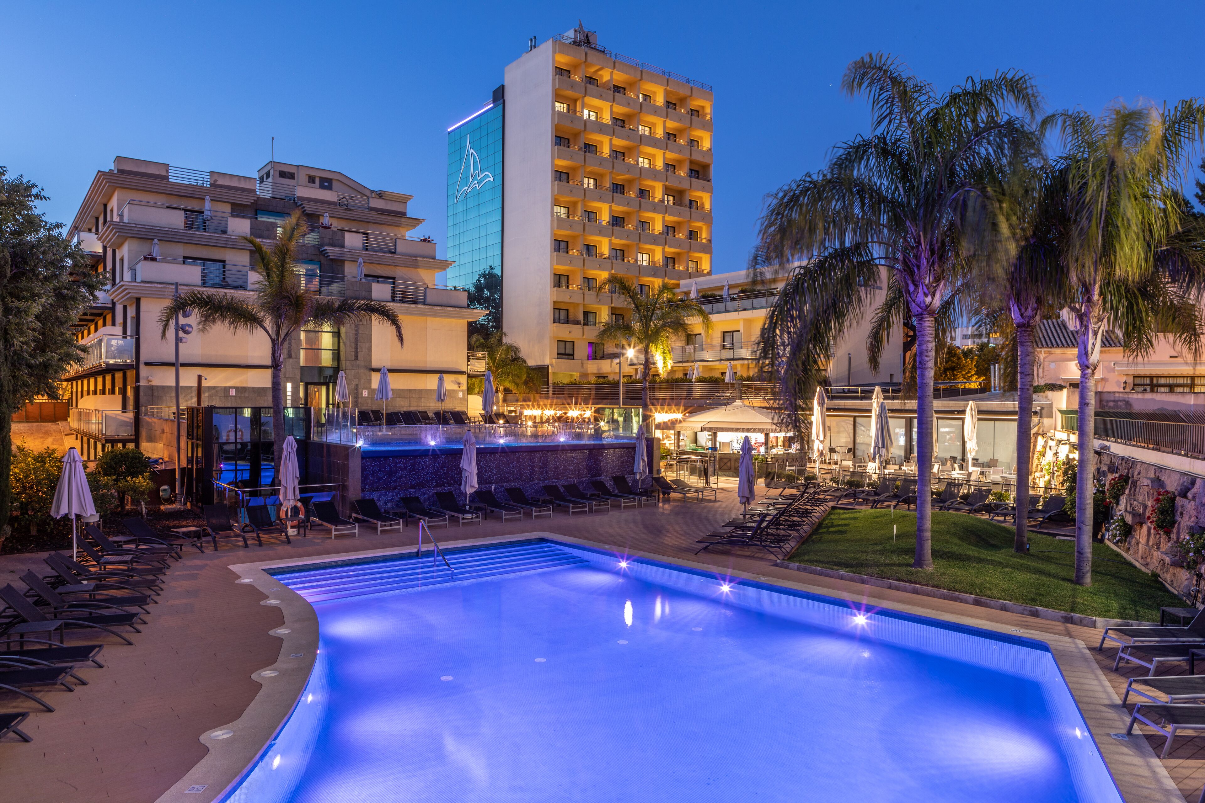 Un hotel con piscina, tumbonas y palmeras.