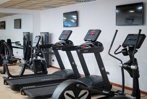 Un gimnasio con cintas de correr, elípticas y una bicicleta estática.