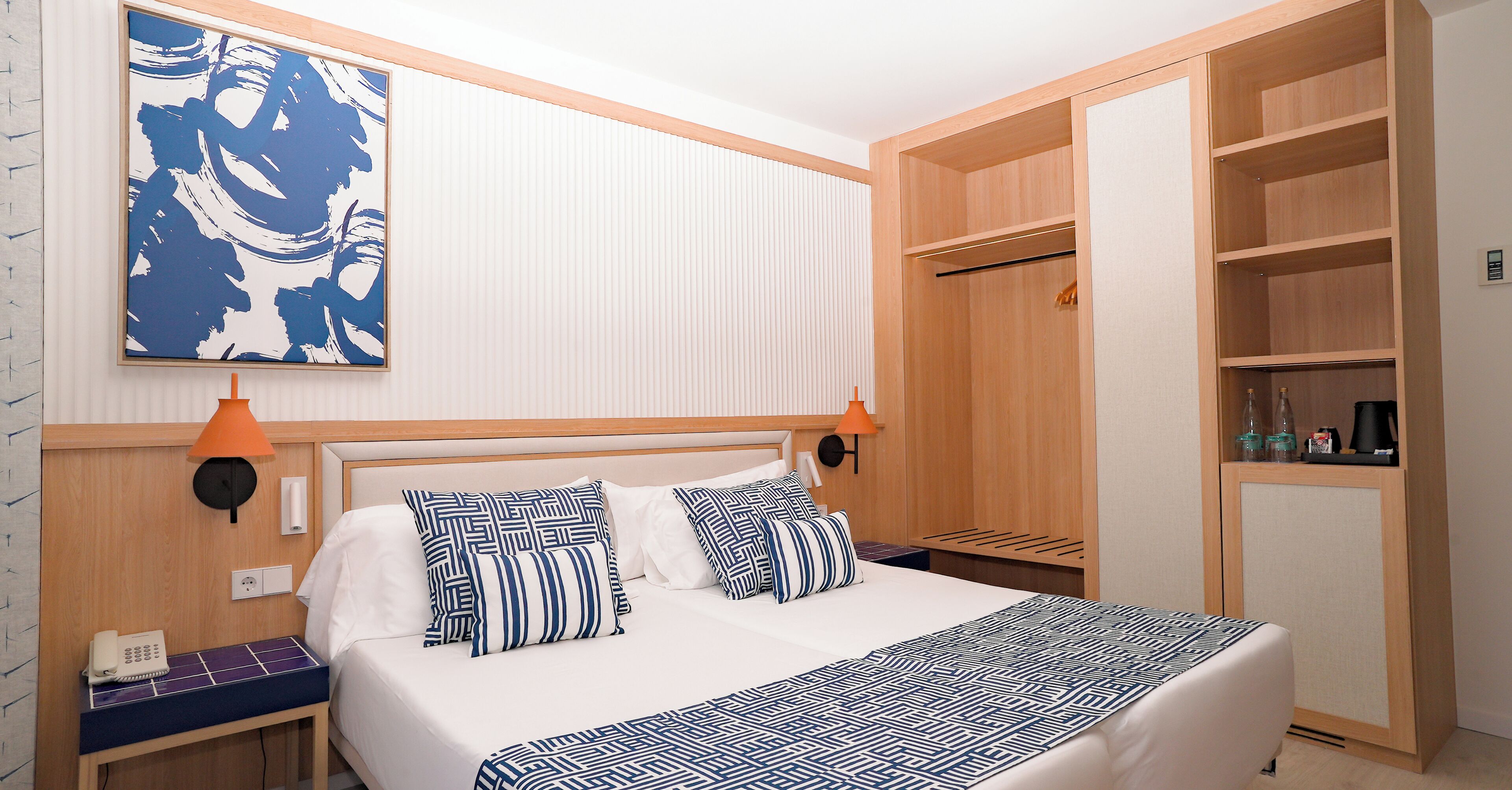 A neatly arranged hotel room with a bed, bedside tables, a wardrobe, and a large abstract painting on the wall.