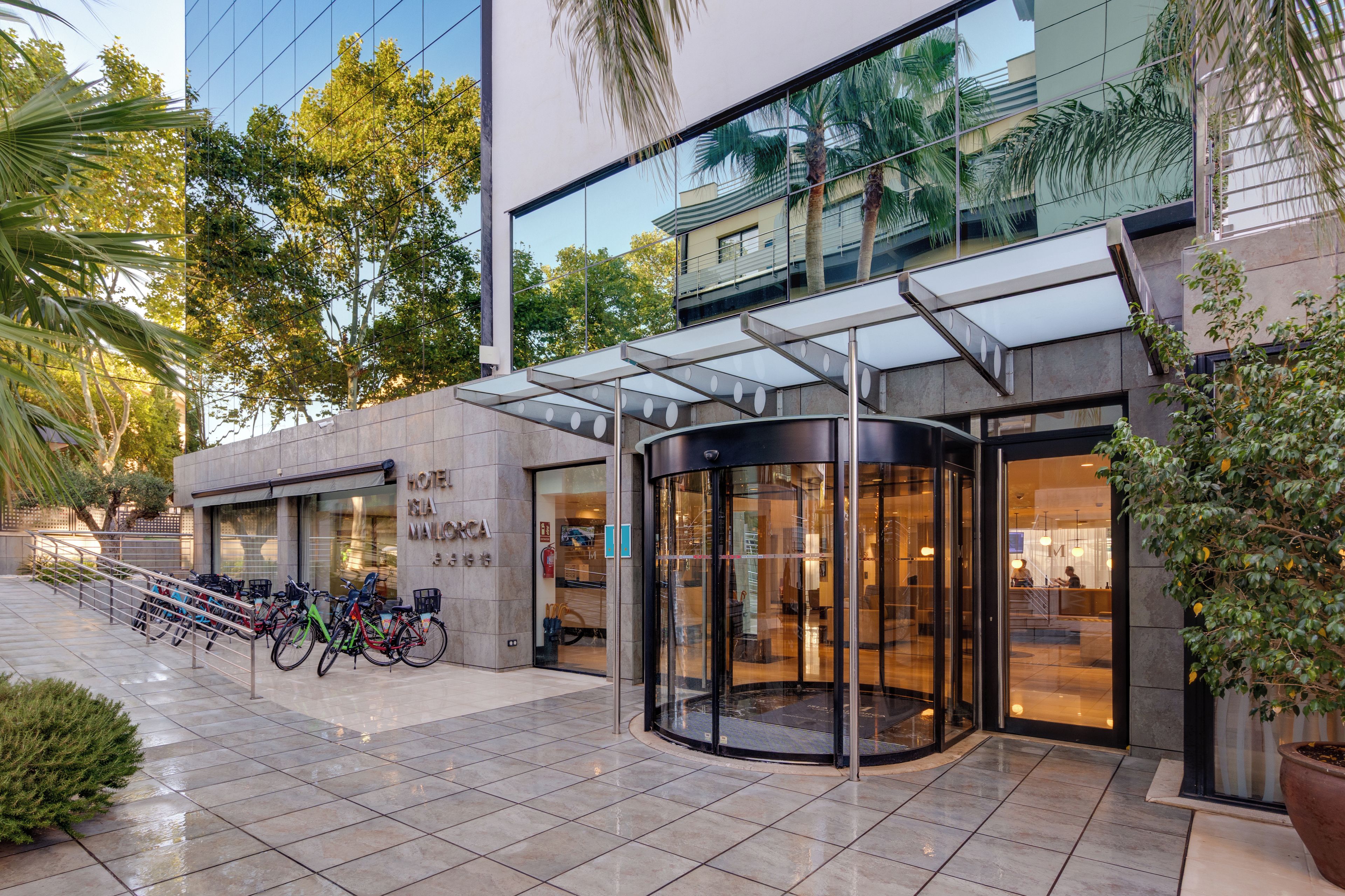 Entrada de un hotel con puerta de vidrio, zona de estacionamiento para bicicletas y fachada de edificio moderno.