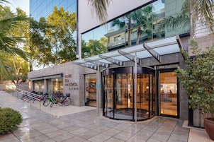 Entrada de un hotel con puerta de vidrio, zona de estacionamiento para bicicletas y fachada de edificio moderno.