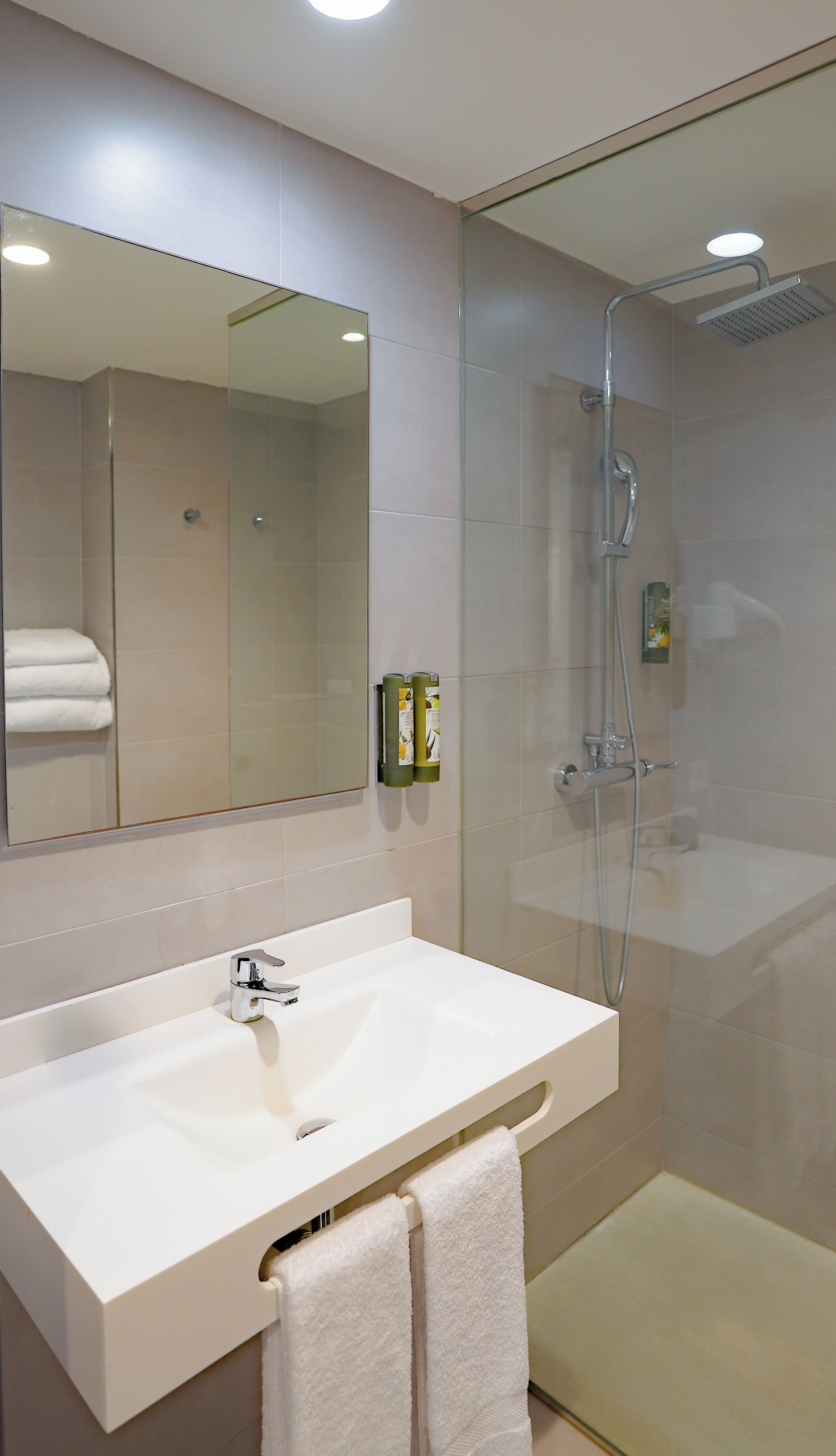 A modern bathroom with a white sink, a large mirror, and a glass-enclosed shower.
