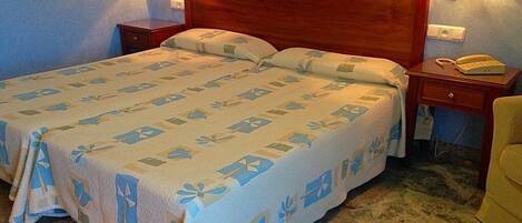 A hotel room with a large bed, wooden headboard, bedside lamps, a telephone, and a small table.