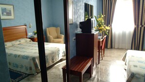 Una habitación de hotel con una cama, una silla, un escritorio con televisor y una ventana con cortinas.