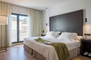Una habitación de hotel con una cama grande, una mesita de noche, una lámpara, una ventana con cortinas y vistas a un edificio.