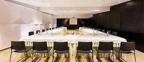 A conference room with a long table, black chairs, and a projector screen.