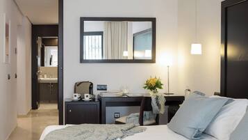 Habitación de hotel con cama, escritorio con computadora, espejo y mesita de noche con lámpara y un florero.