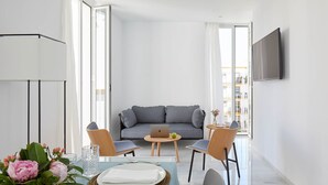 A modern living room with a sofa, a coffee table, and a laptop. There is a dining table with plates and cutlery. - Hotel Fernando III (Seville)