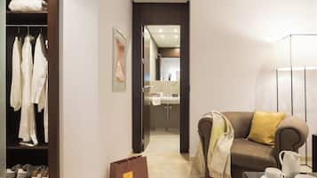 Une chambre d’hôtel avec un placard, un canapé recouvert d’un plaid, une table basse avec une tasse et un bol de biscuits, et une salle de bain visible à travers une porte ouverte.