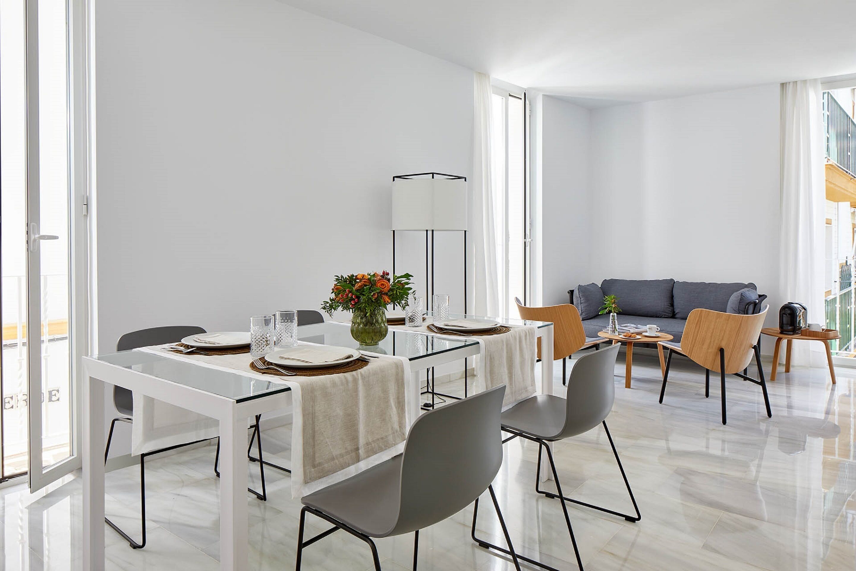 Una sala de estar moderna con zona de comedor, que incluye un sofá, sillas, una mesa preparada para comer y una lámpara de pie.
