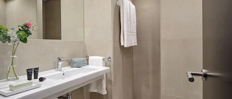 A modern bathroom with a white sink, a mirror, a towel rack, and a shower area.