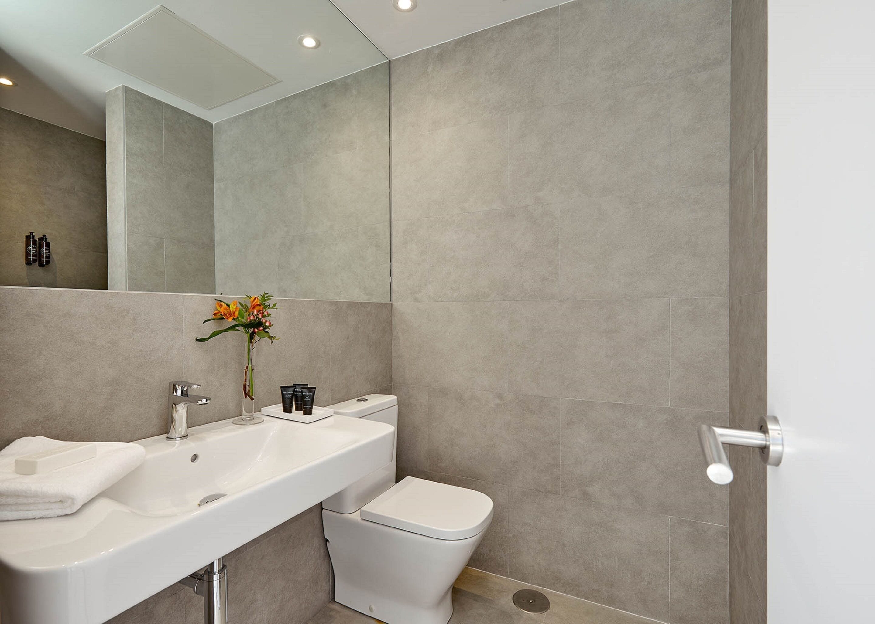 Un baño moderno con un espejo grande, dos lavamanos, un inodoro y una zona de ducha.