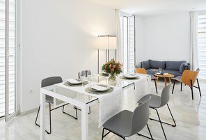 Un comedor moderno con una mesa blanca, sillas grises y un jarrón con flores.
