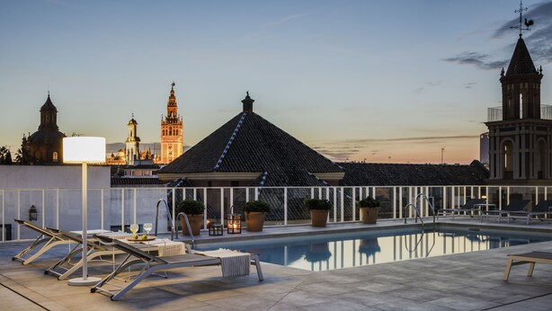 A rooftop pool area with lounge chairs, a swimming pool, and a view of historic buildings. - Hotel Fernando III (Seville)