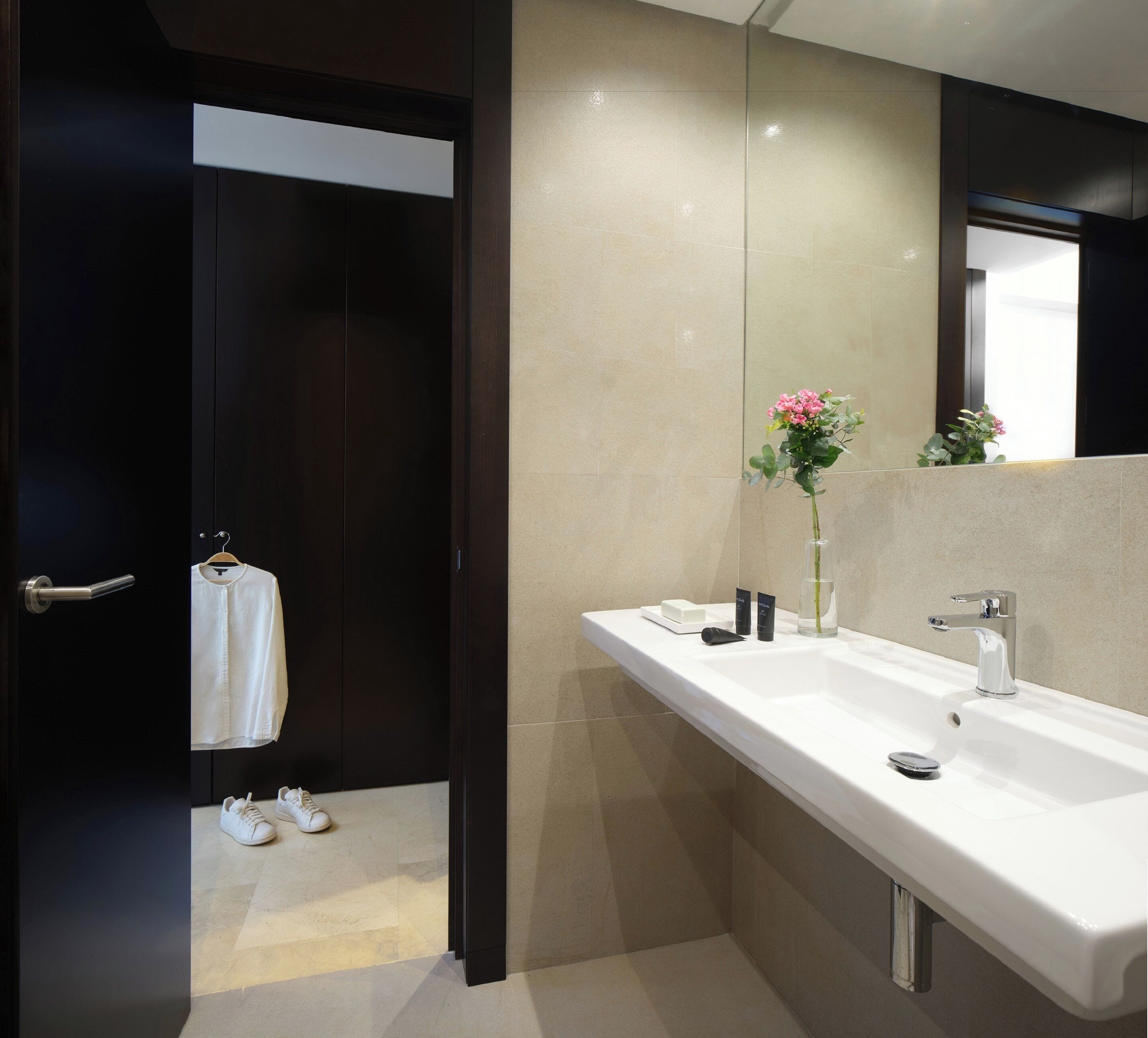 Une salle de bain moderne avec un grand miroir, un lavabo blanc et une porte en bois foncé.