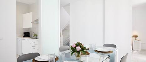 Un comedor moderno con una mesa de vidrio, sillas blancas y un jarrón con flores.