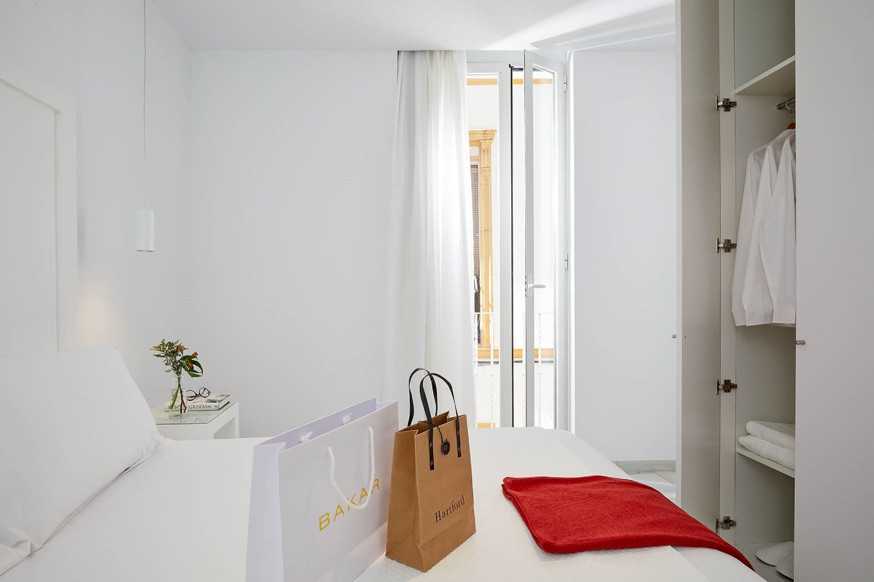 Una habitación de hotel con cama, mesita de noche con un florero y vasos, una toalla roja y un armario.