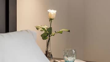 A bedroom with a bed, a bedside table with a vase of flowers, and a pendant light.