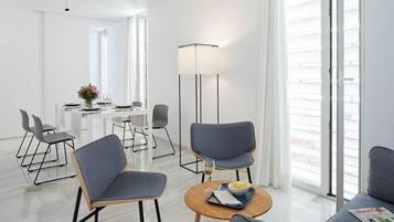 Una habitación de hotel moderna con zona de comedor, sofá y una lámpara de pie.