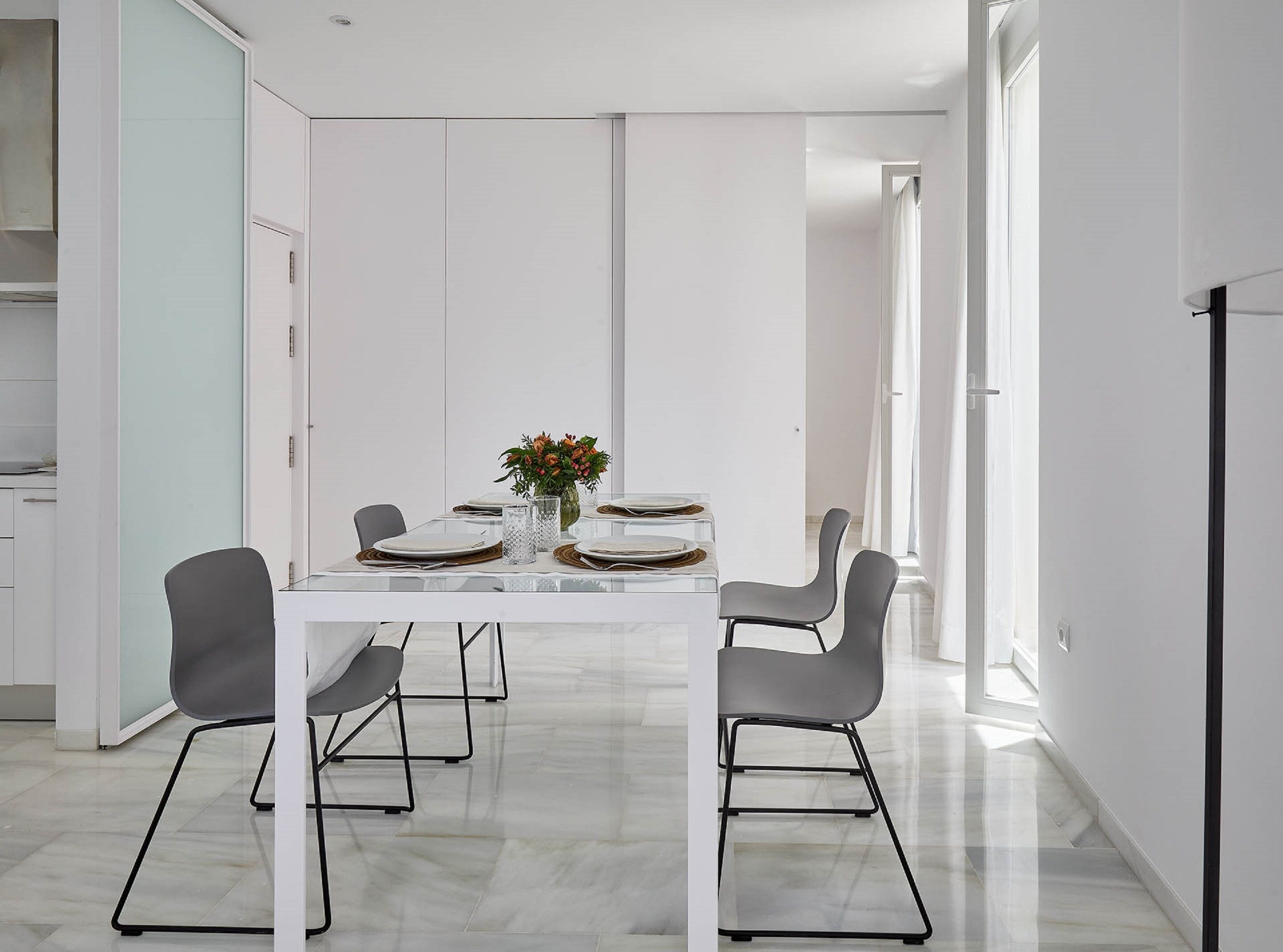 Un comedor moderno con una mesa blanca dispuesta para cuatro personas, rodeada de sillas grises.