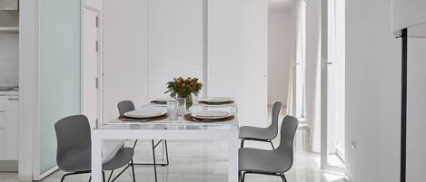 Un comedor moderno con una mesa blanca dispuesta para cuatro personas, rodeada de sillas grises.