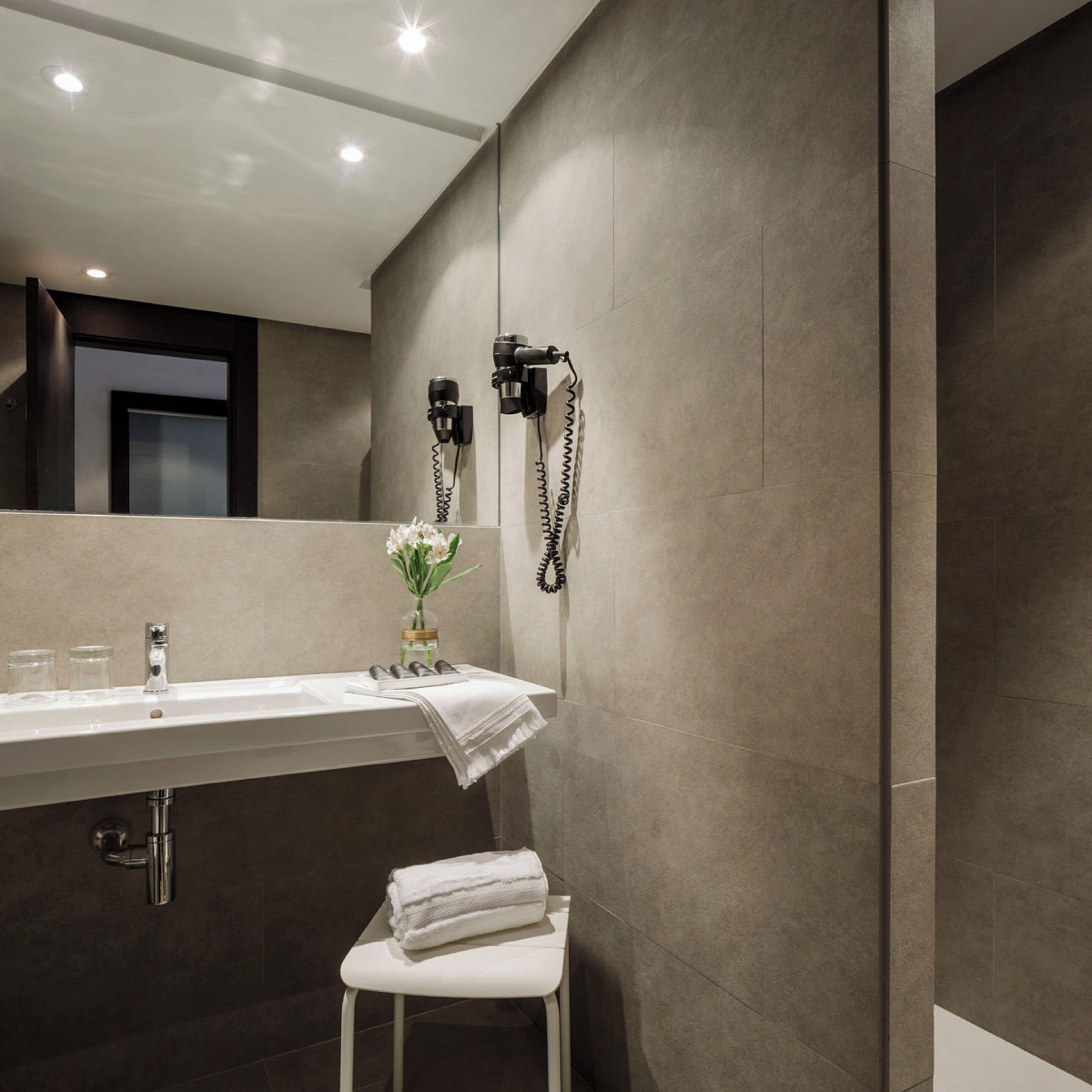 A modern bathroom with a large mirror, a sink, and two hair dryers mounted on the wall.