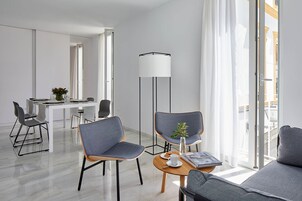 Una habitación de hotel moderna con zona de comedor, un sofá y una lámpara de pie.