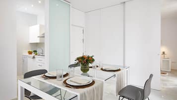Un comedor moderno con una mesa de vidrio, paredes blancas y una cocina al fondo.