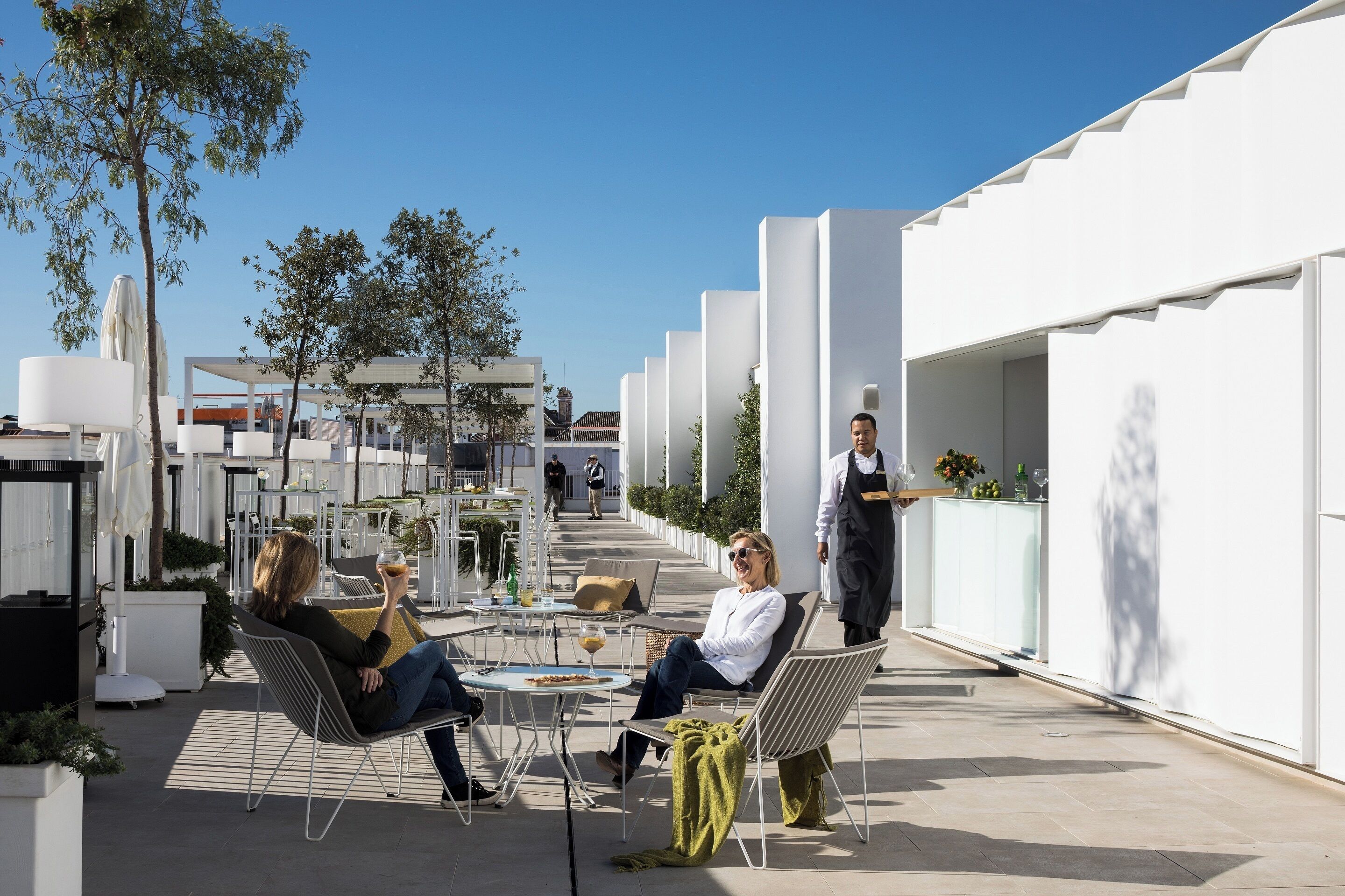 An outdoor seating area with modern chairs and tables, surrounded by white walls and trees.