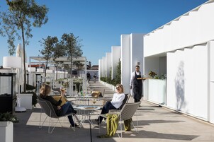 An outdoor seating area with modern chairs and tables, surrounded by white walls and trees.