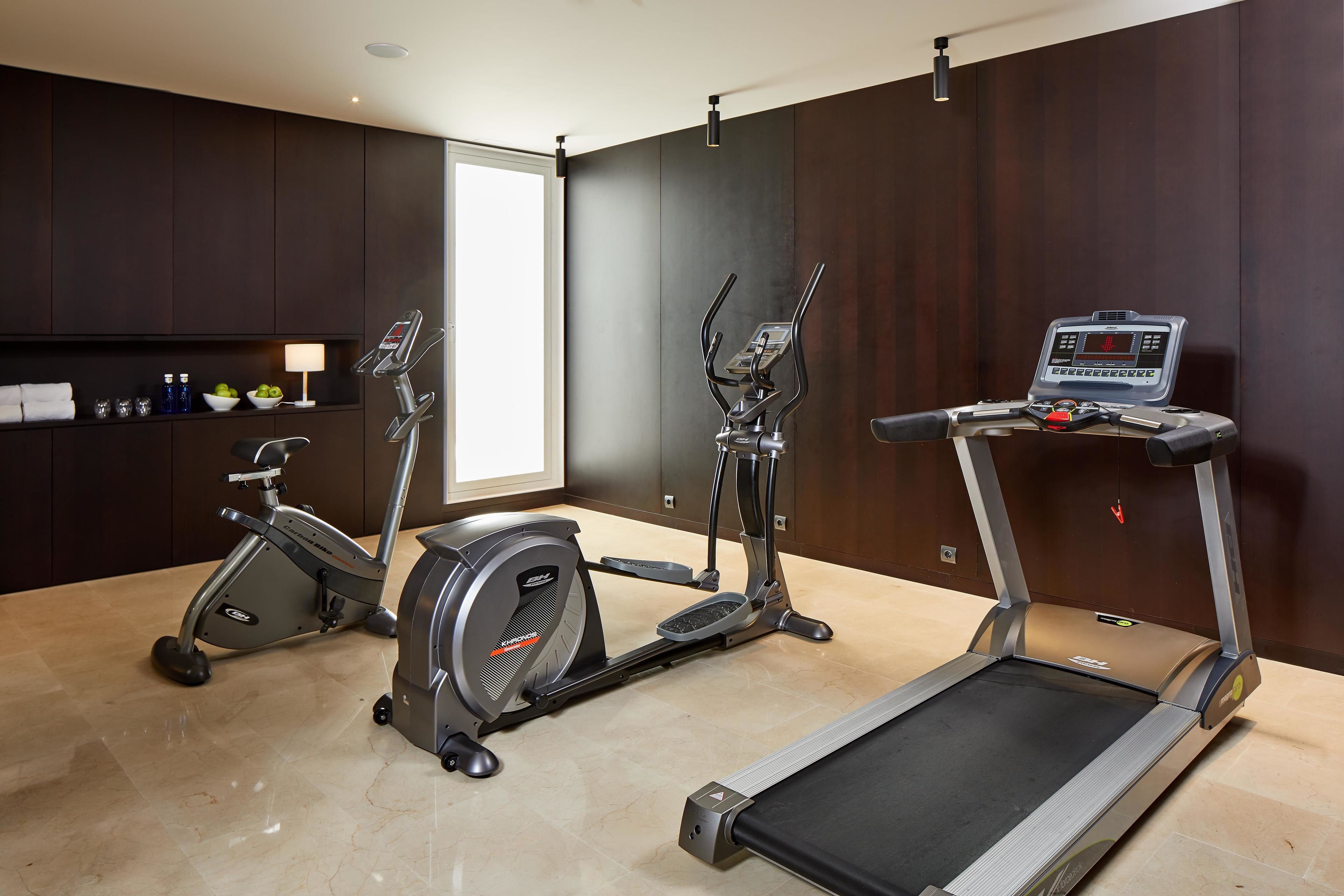 Un gimnasio en casa con cinta de correr, elíptica y bicicleta estática.