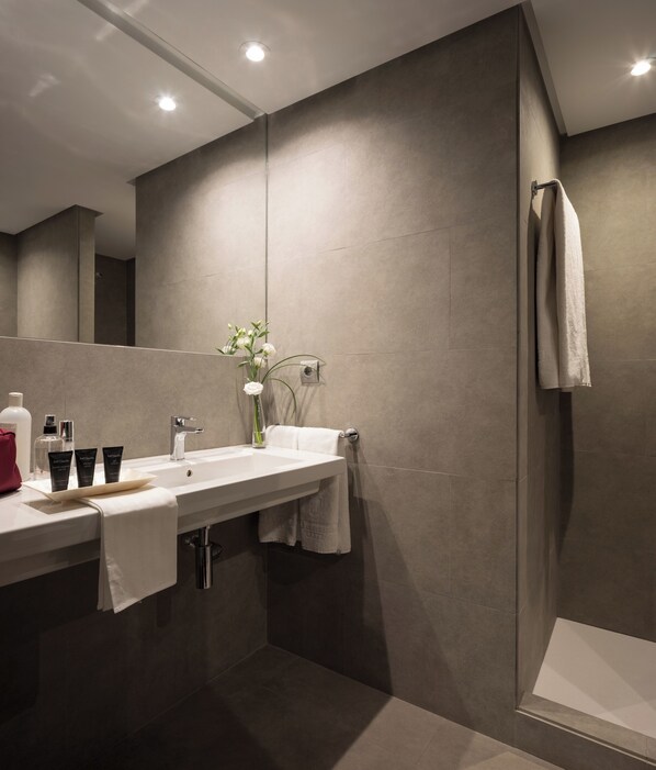 A modern bathroom with a large mirror, a sink with toiletries, and a shower area. - Hotel Fernando III (Seville)