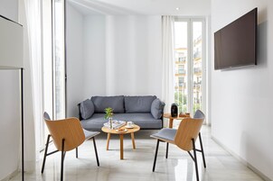 A modern living room with a grey sofa, two wooden chairs, a small round table with a plant, a coffee cup, and a remote control.