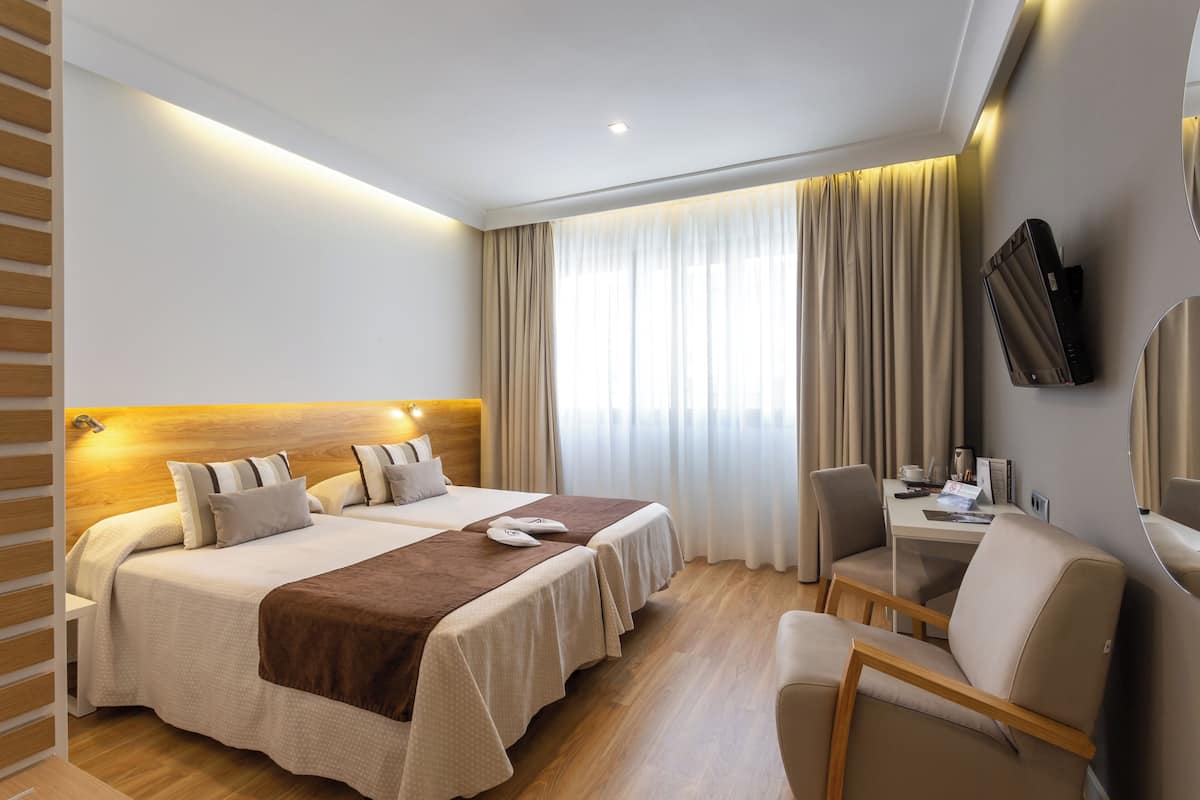 Habitación de hotel con una cama grande, un escritorio, una silla y un televisor montado en la pared.