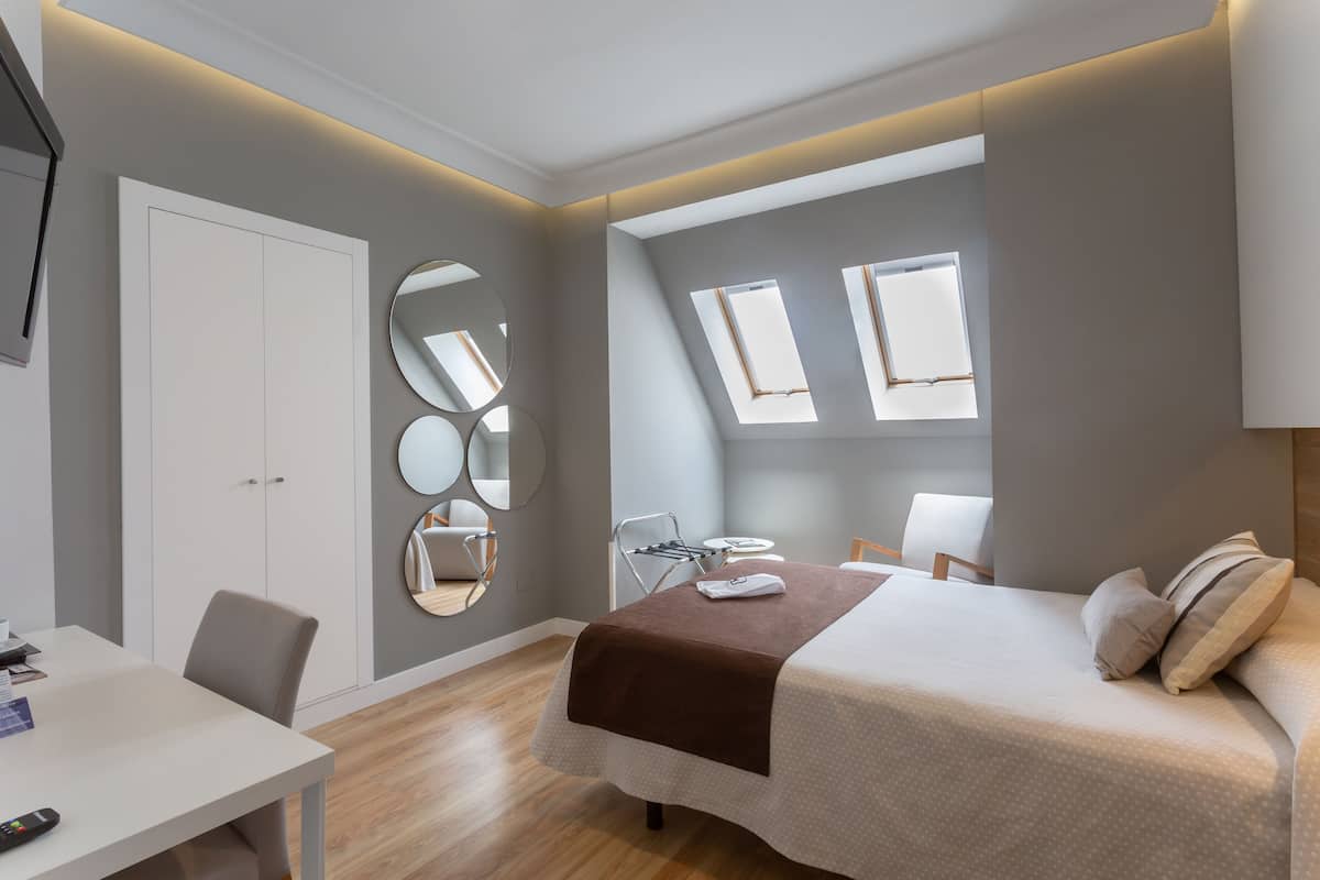 Un dormitorio moderno con cama, escritorio y silla. Hay dos ventanas y una lámpara en el techo.