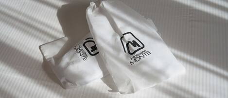 Deux sacs blancs ornés du logo « HOTEL MONTE » sur une surface en tissu à rayures.