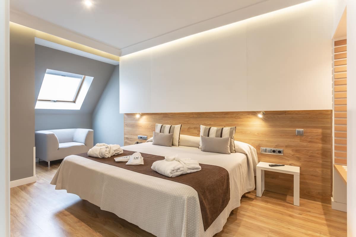 Habitación de hotel moderna con una cama grande, una mesita de noche pequeña, una silla y un tragaluz.