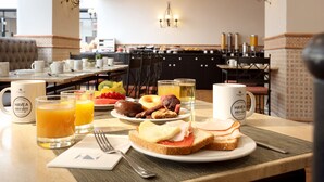 A breakfast setting with a table set for two, including plates with toast, eggs, and fruit, and two glasses of orange juice.