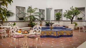 A courtyard with white ornate furniture, a tiled fountain, and potted plants.