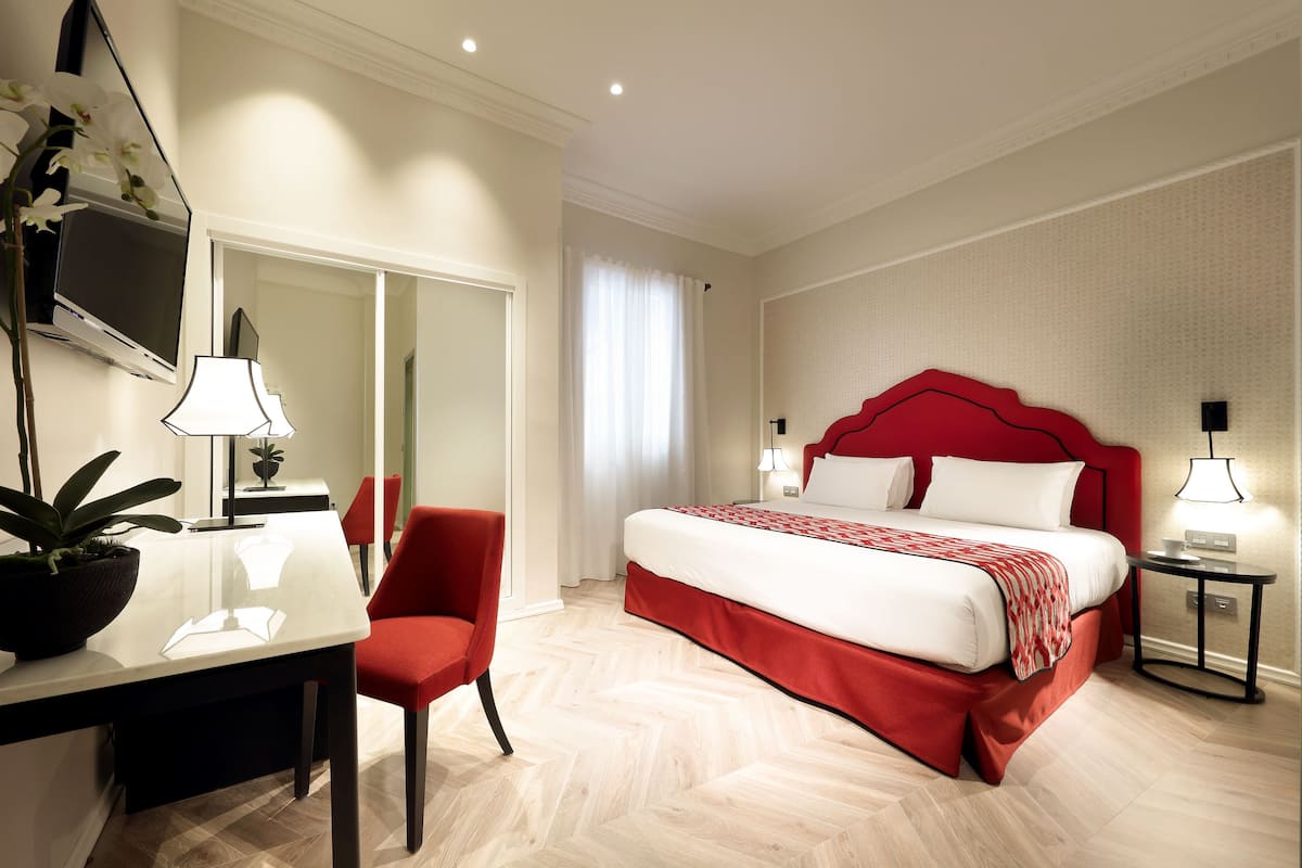 Ein Hotelzimmer mit einem großen Bett, einem Schreibtisch mit Stuhl, einem Fernseher und einer Zimmerpflanze.