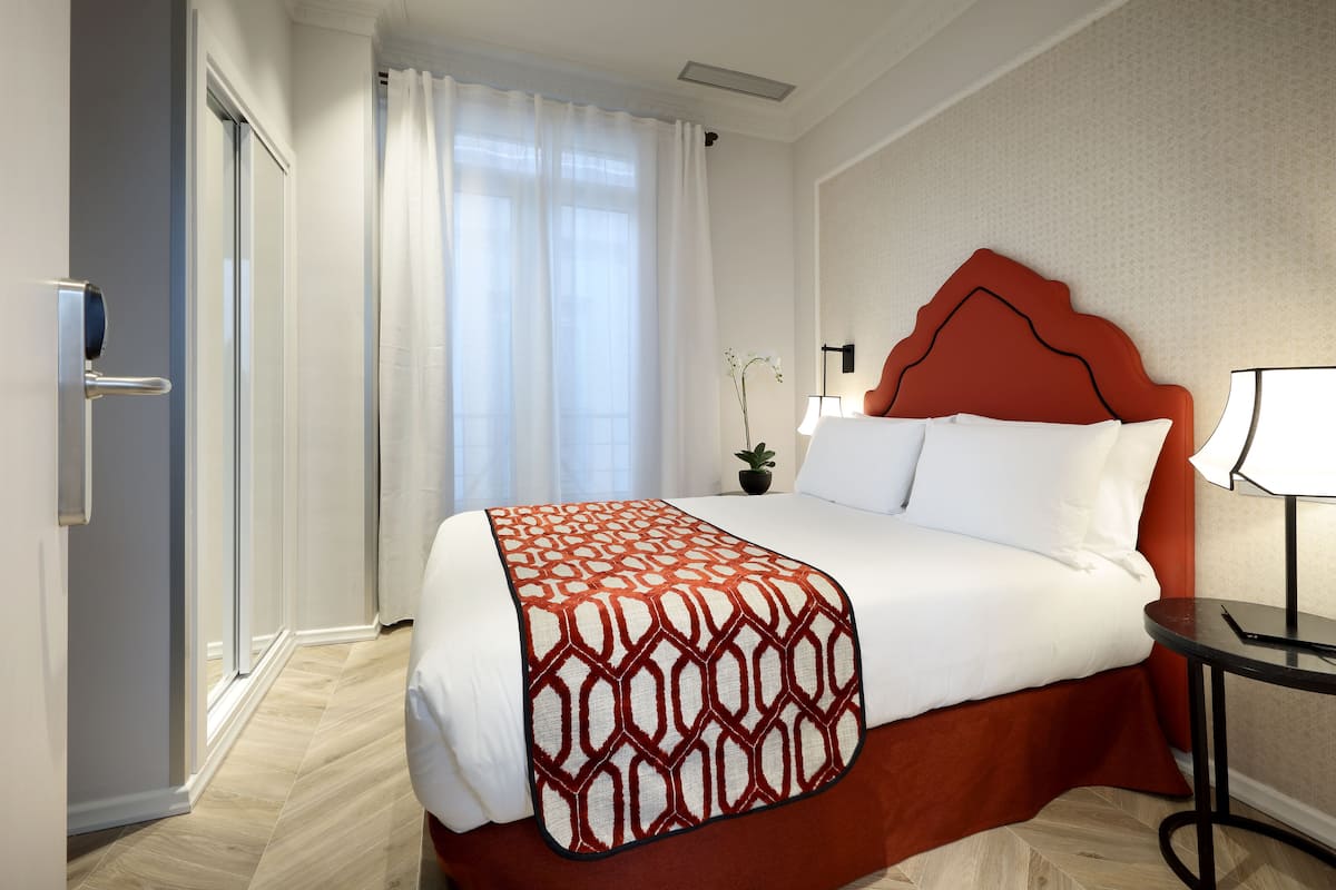 Ein Hotelzimmer mit einem Bett, einem Nachttisch, einer Zimmerpflanze und einer Tür.