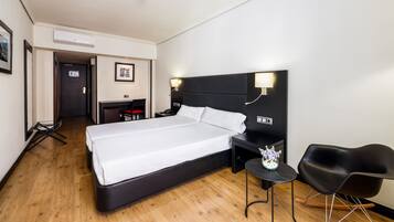A hotel room with a large bed, a desk, a chair, and a small table with a vase.