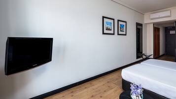 Een hotelkamer met een flatscreen televisie, een bed, een kleine tafel met een bloevas en twee ingelijste foto’s aan de muur.