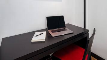 Un escritorio con una computadora portátil, un cuaderno y un bolígrafo. Encima de la pared, hay un cuadro enmarcado.